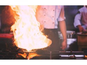 Μάγειρας κρατάει τηγάνι με φωτιά στο χέρι